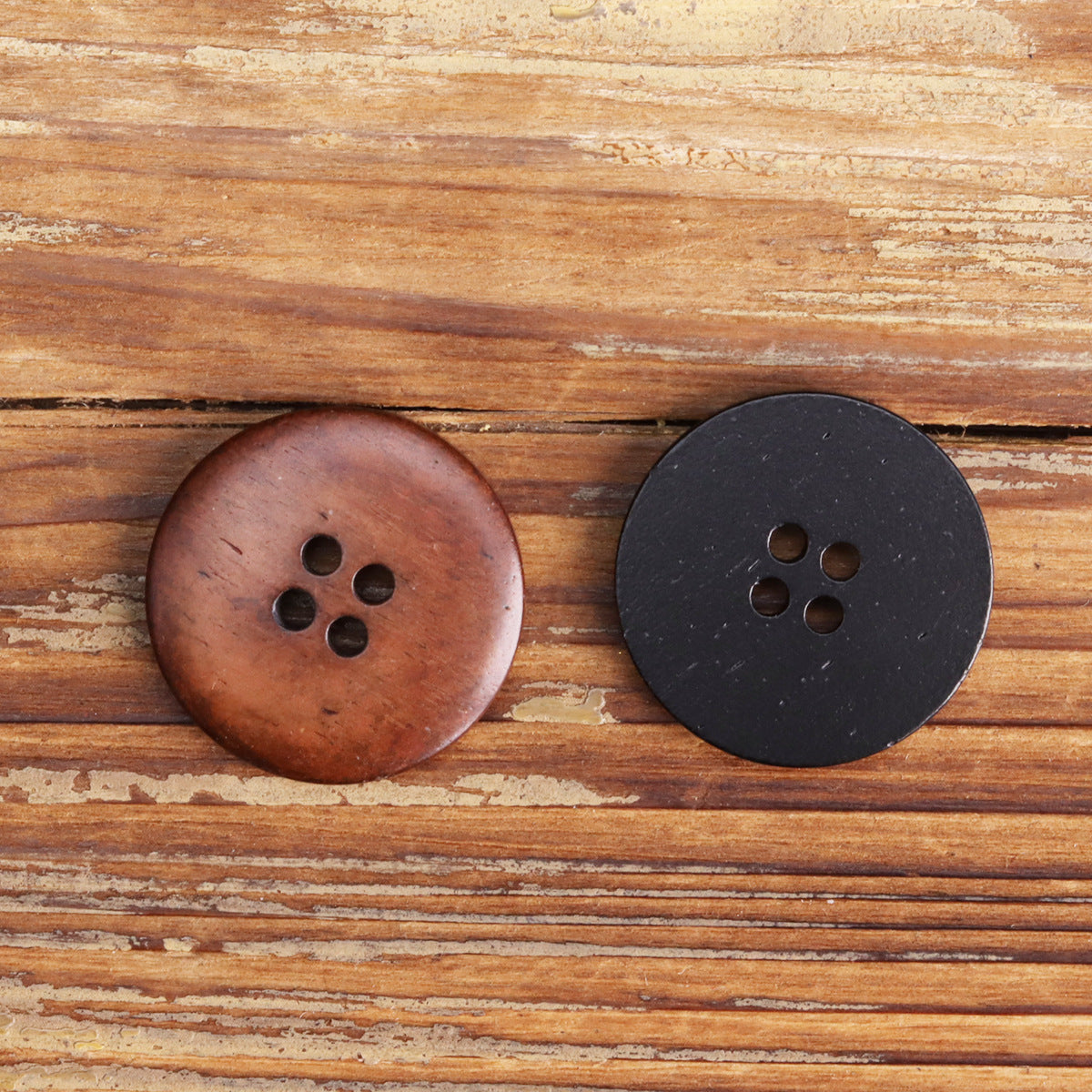 Black flat four-hole button, round face with four stitch holes, dark finish.