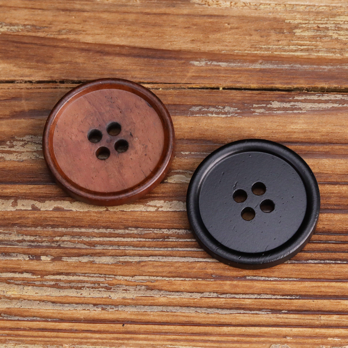 Black four-hole button on wood, dark matte finish, front side with four holes.