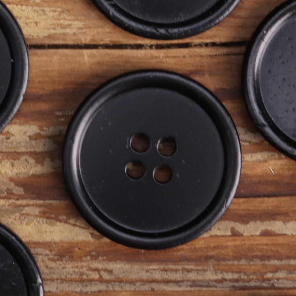 Close-up of black four-hole button, round face and raised edge with four holes.
