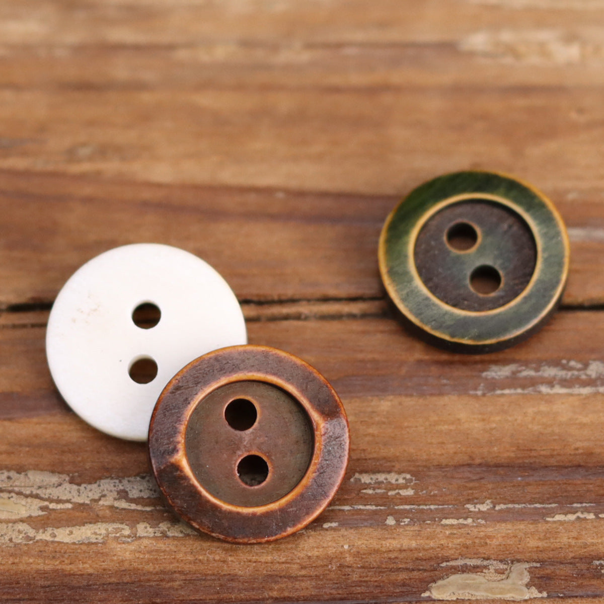 White, green, and brown round two-hole shirt buttons with bronze-toned edges