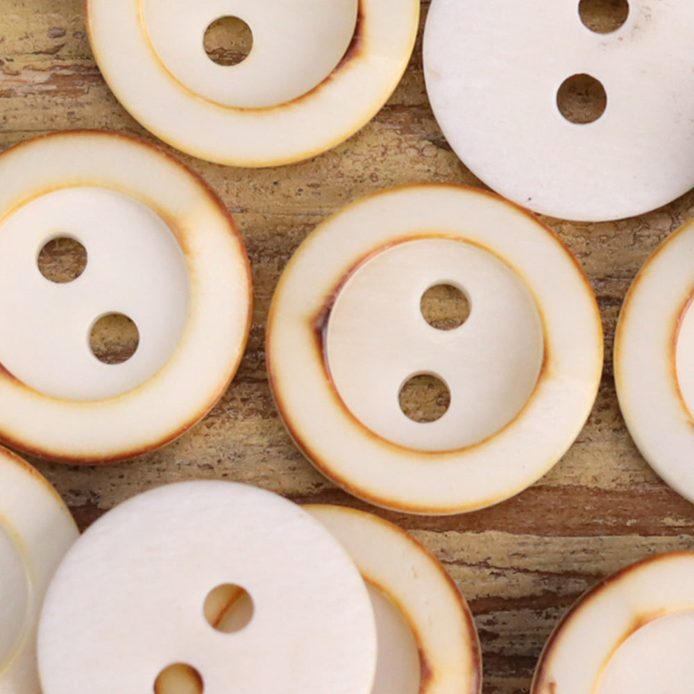 White round two-hole shirt buttons with warm beige outer border, close-up
