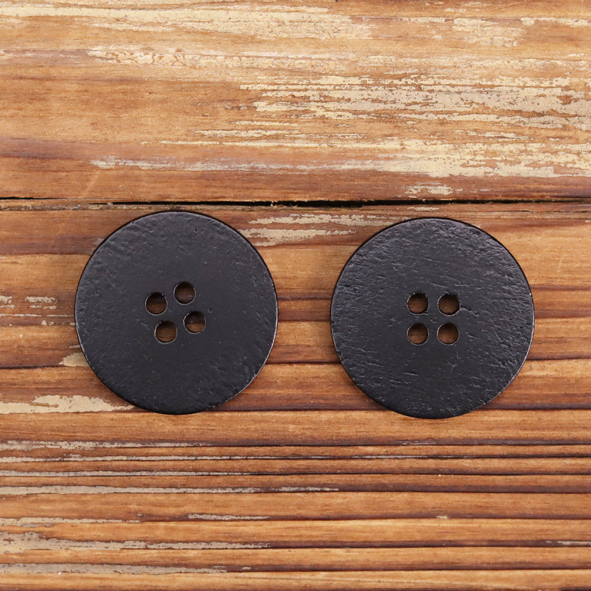 Two black round four-hole buttons, flat faces and clean rounded border