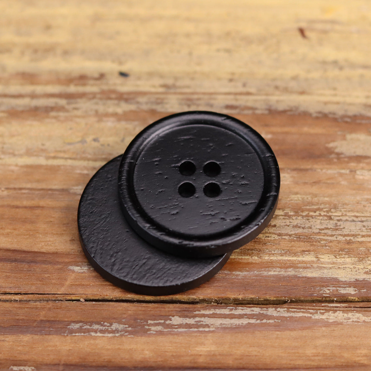Black four-hole round button with textured surface and smooth rim