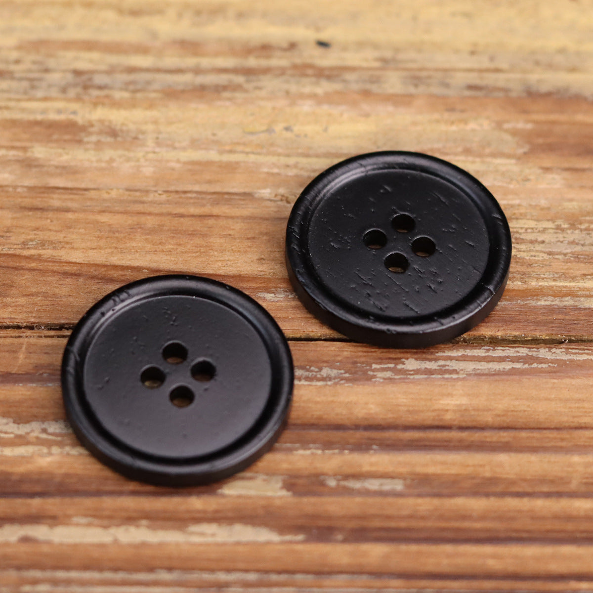 Pair of black round four-hole buttons with subtle textured finish