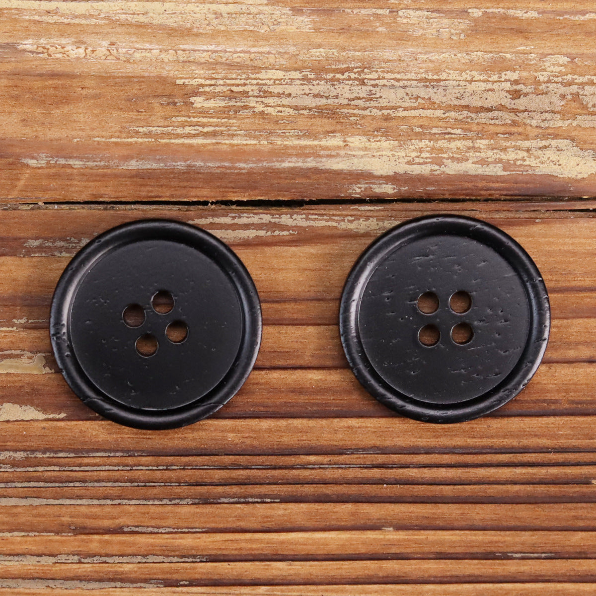 Two black round buttons with four holes, matte look, rounded edges