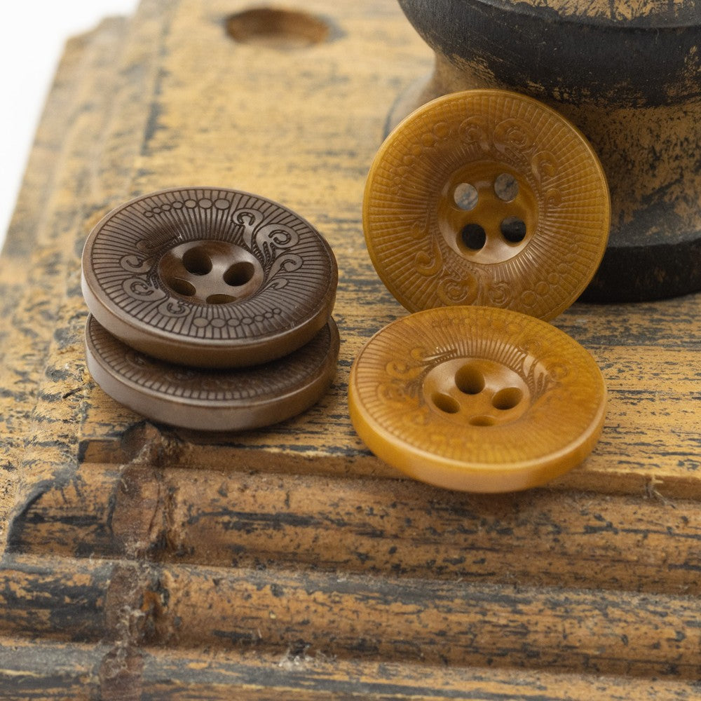 Yellow four-hole nut shell button with etched swirl pattern; brown button in back