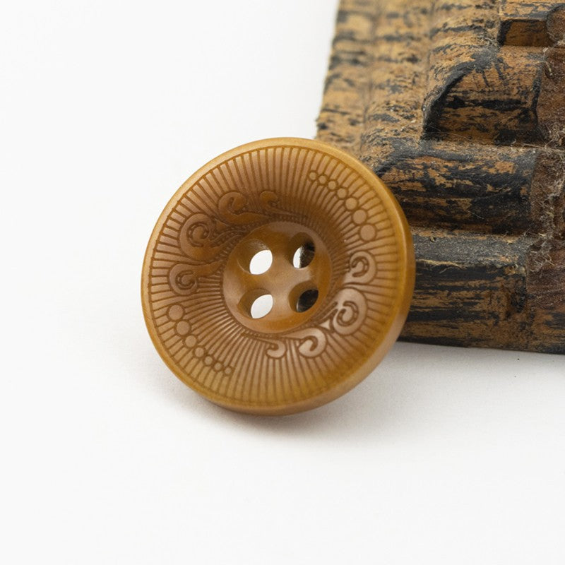 Yellow four-hole nut shell button with decorative etched mandala pattern