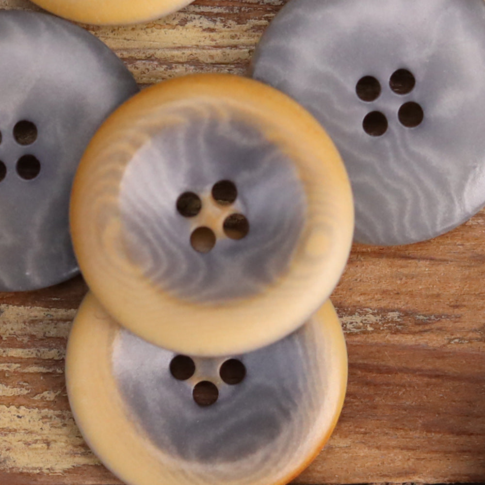 Yellow-tan and gray round nut shell button with 4-hole design in close-up