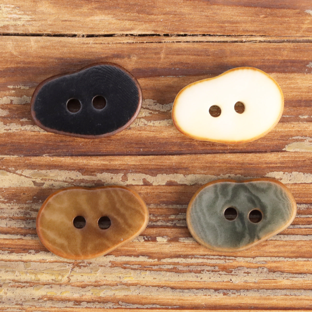 Assorted peanut-shaped fruit buttons: dark, cream, and gray-blue, each with 2 holes