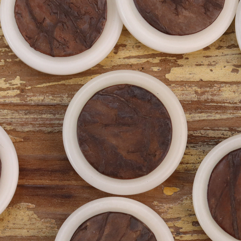Close-up of round corozo buttons with white rims and dark brown wood grain