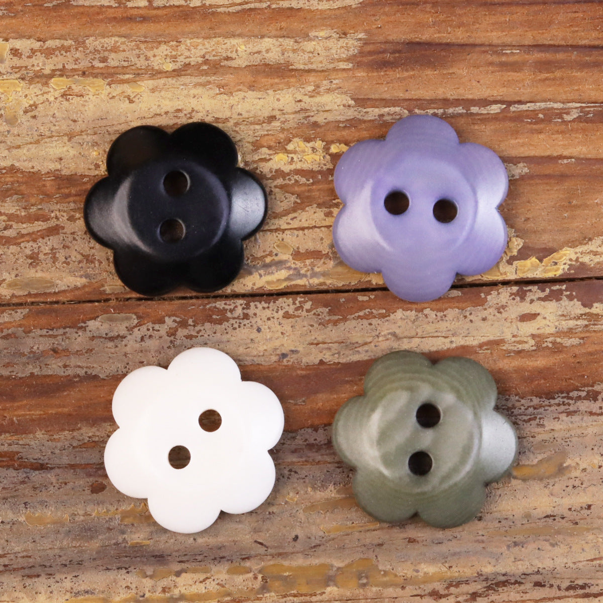Assorted flower-shaped corozo buttons in black, lavender, white, and olive, two holes each.