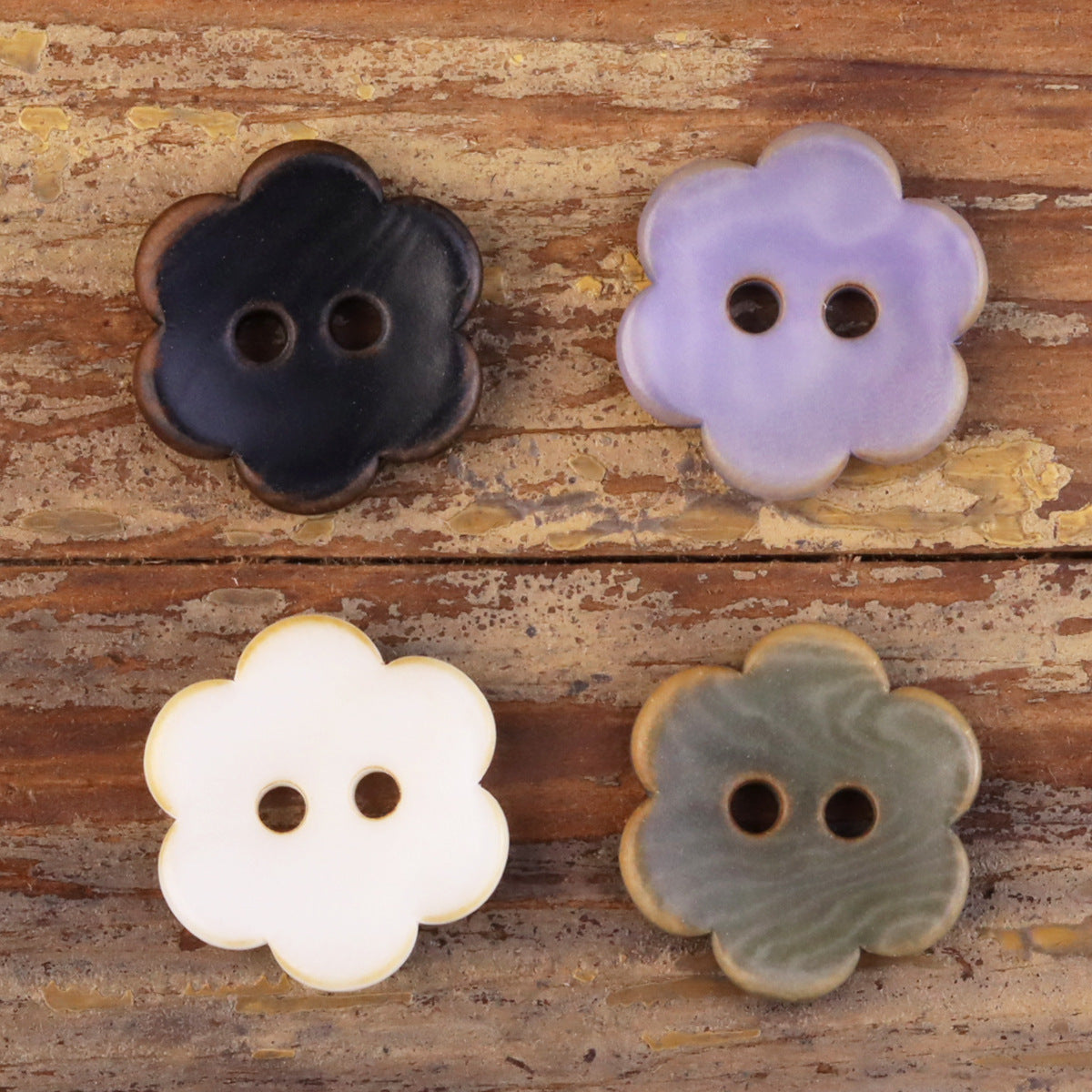Flower-shaped corozo buttons set: dark, lavender, white, and gray tones, each with two holes.