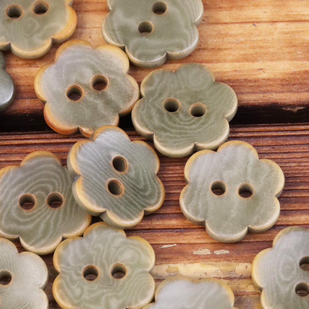 Gray-olive flower-shaped corozo buttons with two holes, pale edges visible.