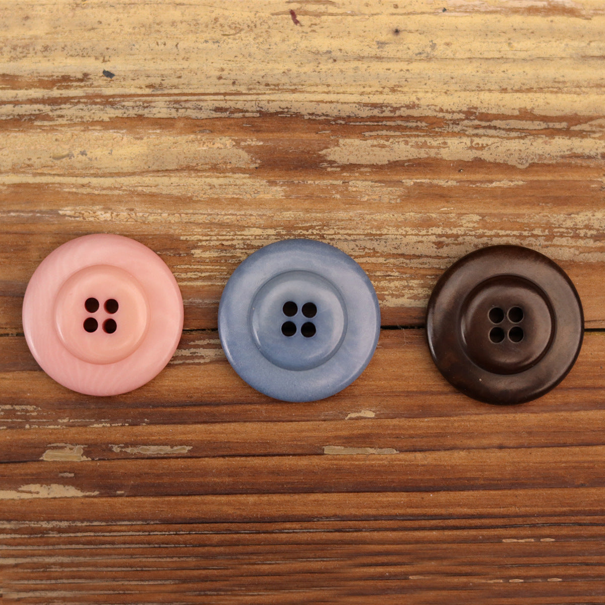 Three round corozo buttons: pink, blue, and coffee, each with four holes
