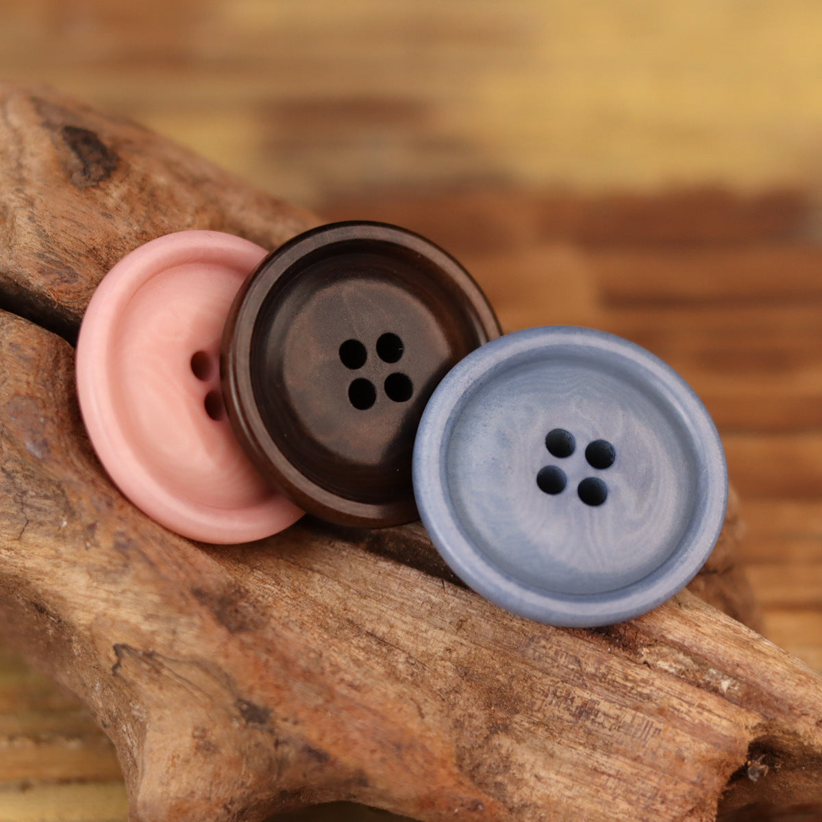 Close-up of three round corozo buttons in pink, coffee, and blue, four holes