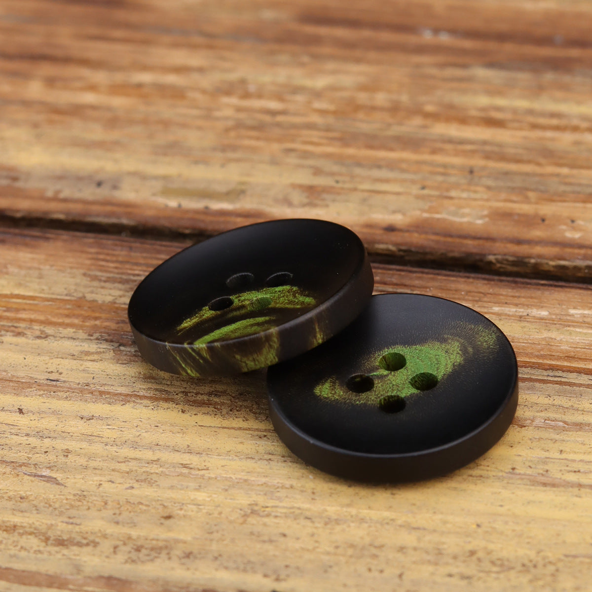 Pair of dark 4-hole buttons showing green floral motifs from side angle.