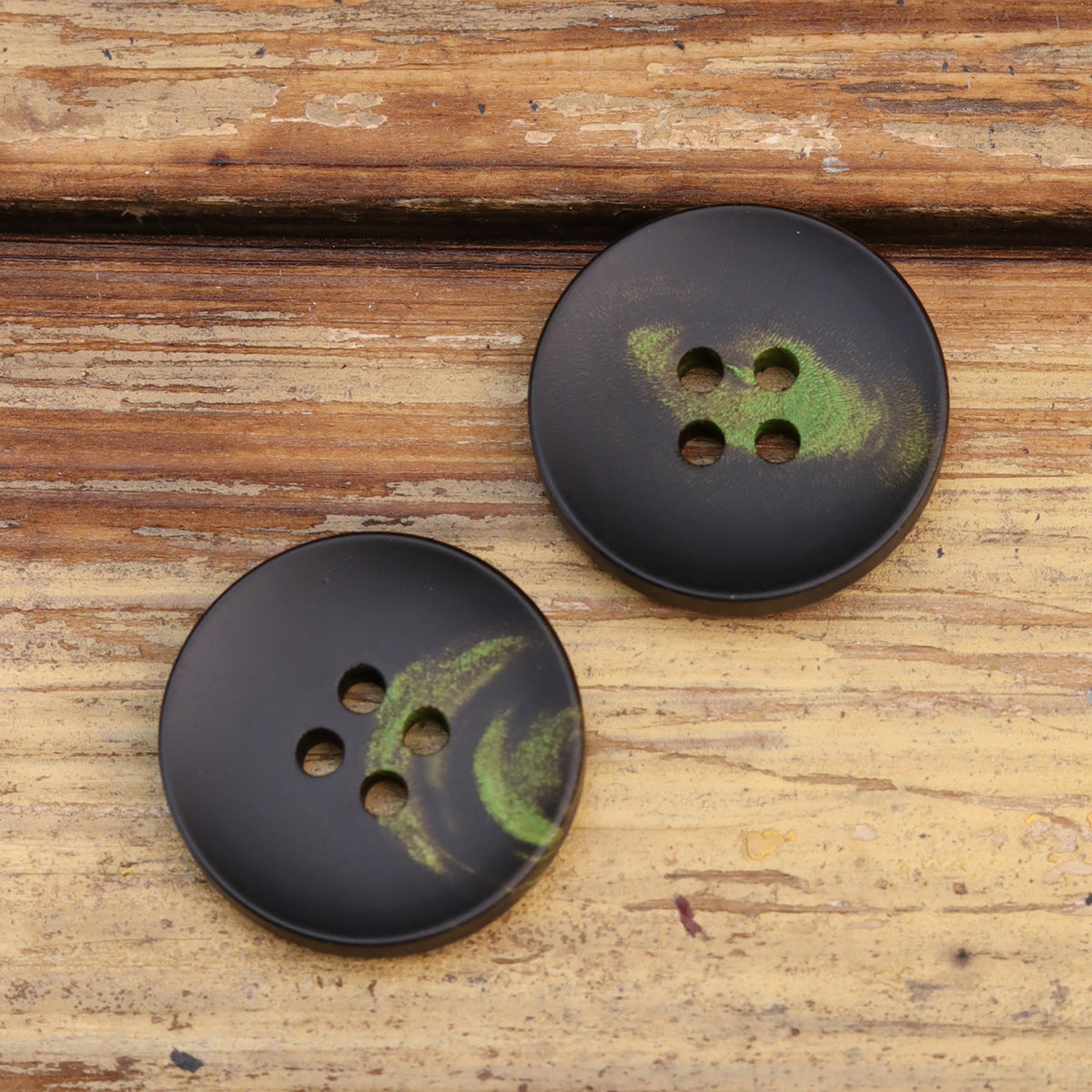 Two dark 4-hole buttons with green floral pattern in different sizes.