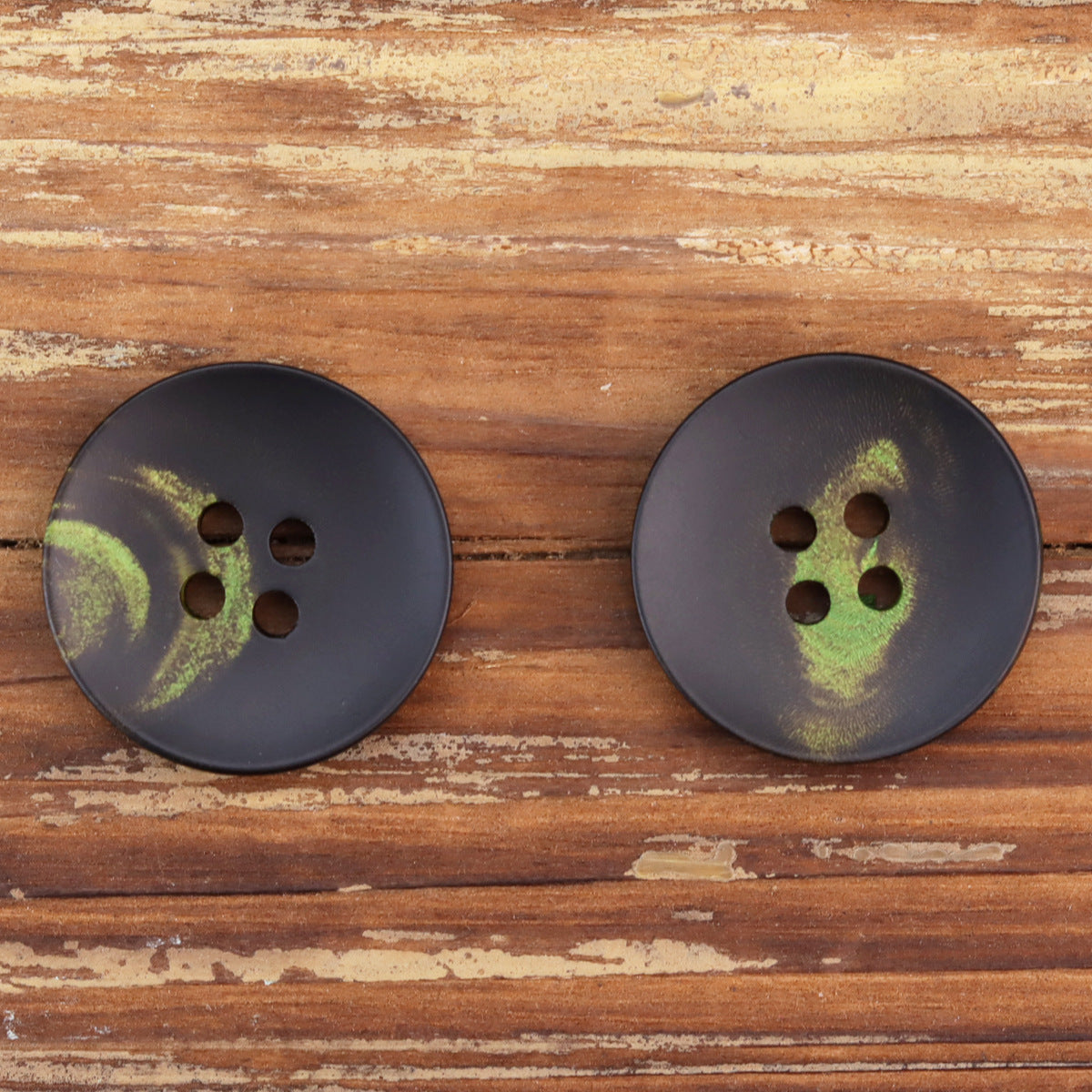 Two dark round 4-hole buttons with green floral design, front view.