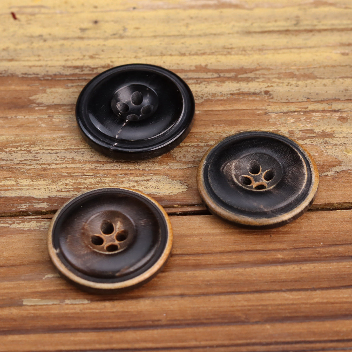 Three horn buttons in dark shades with four holes and tan outer rim
