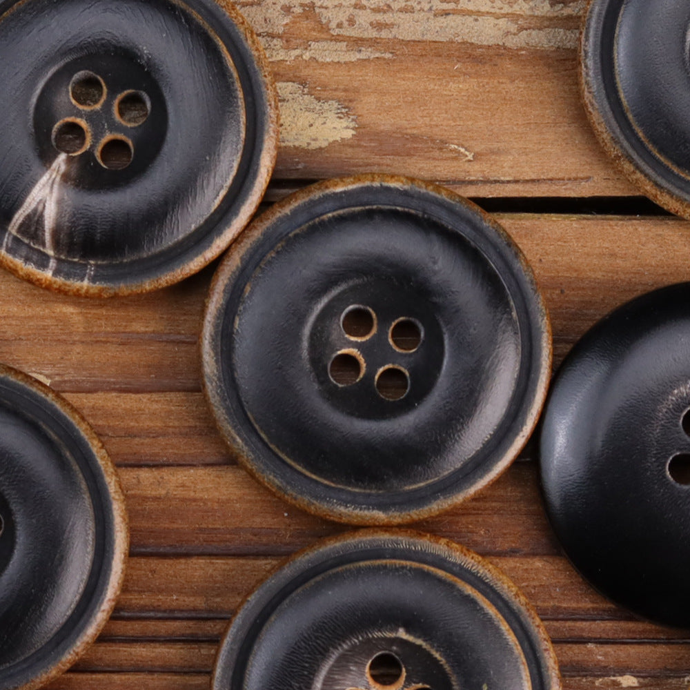 Close-up of four-hole black horn buttons with burnished surface and tan edge