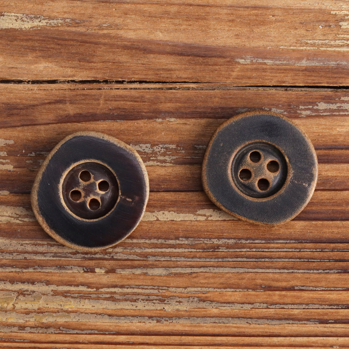 Irregular burnished horn buttons with four holes, dark finish, front view, pair