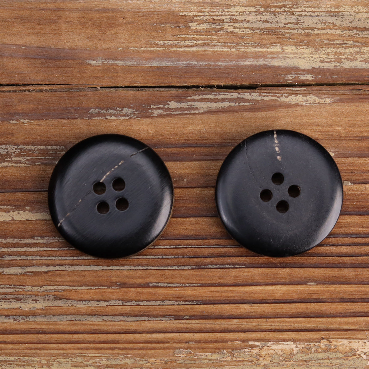 Black four-hole horn buttons with smooth circular face and slight sheen