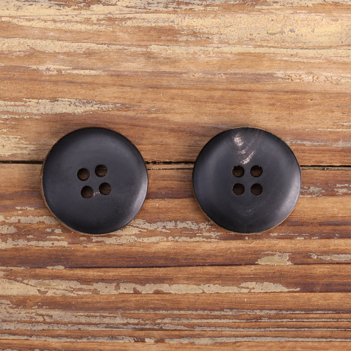Two dark round buttons with four holes, smooth matte finish