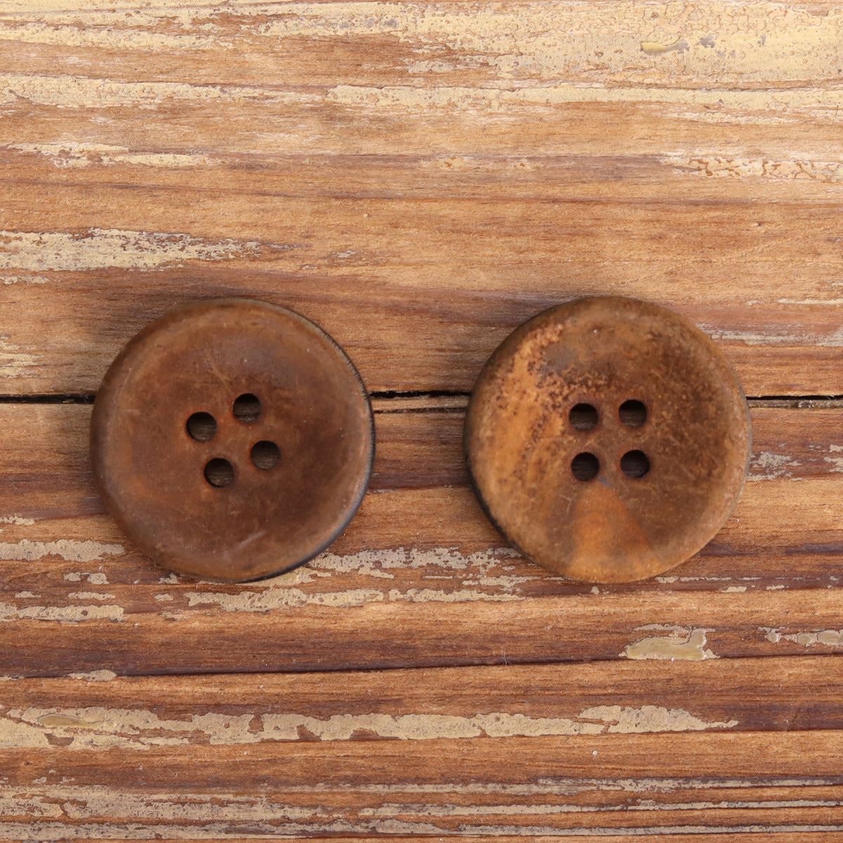 Two round dark horn buttons with four-hole design on wooden background