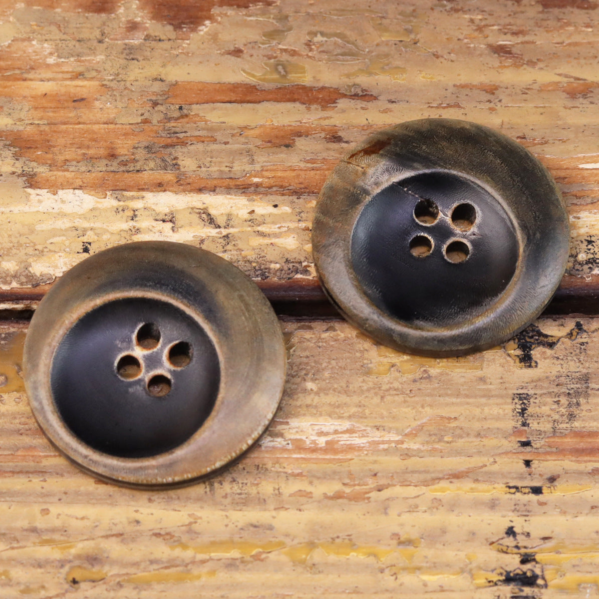 Two round burned black horn buttons, bronze-washed rim, four sew holes