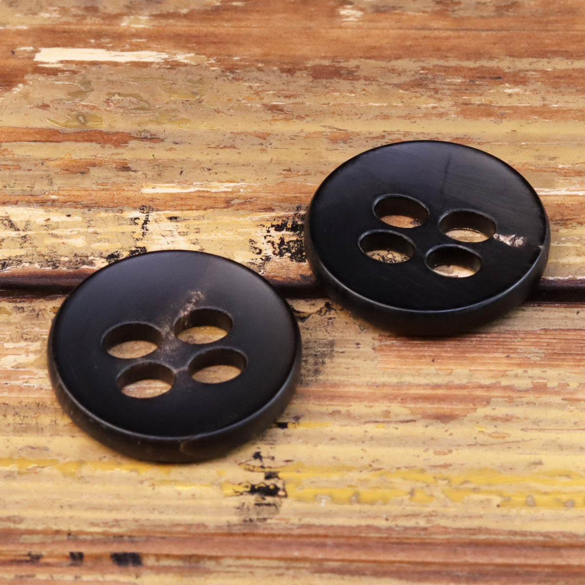 Black round 25mm four-hole buttons, two pieces with large eyelets visible