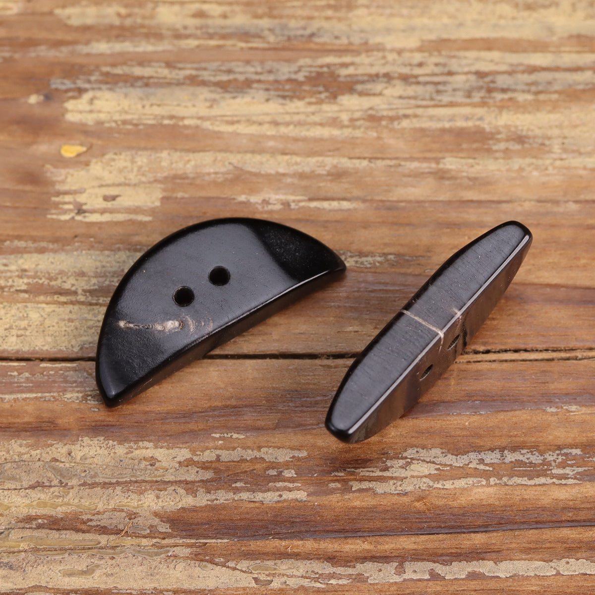Pair of black horn buttons, irregular triangular half-moon shape, round holes