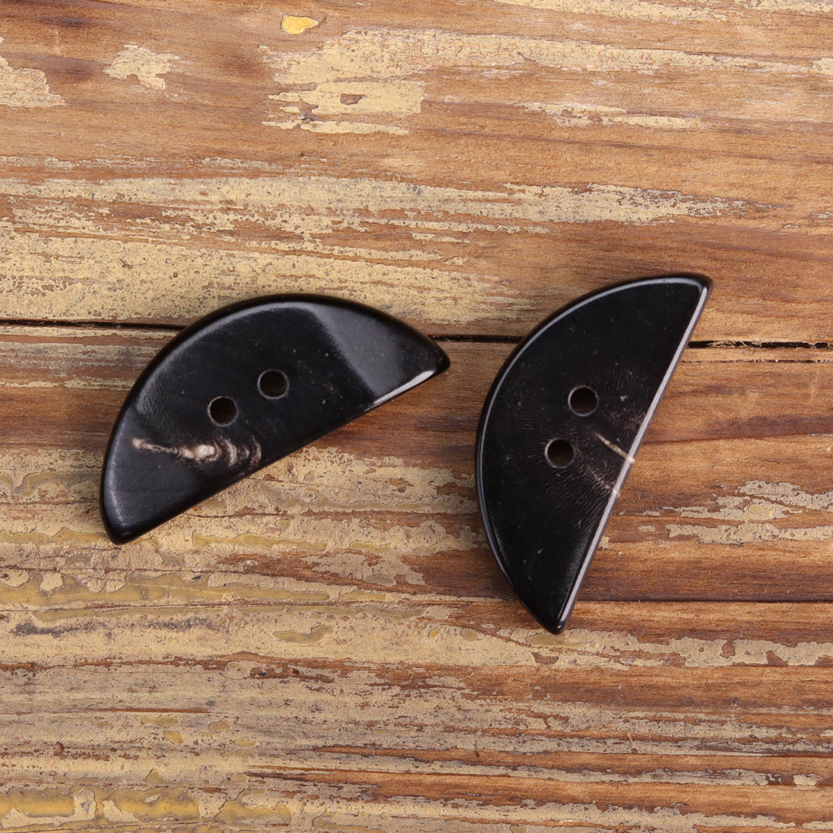 Two black triangular half-moon horn buttons with round holes