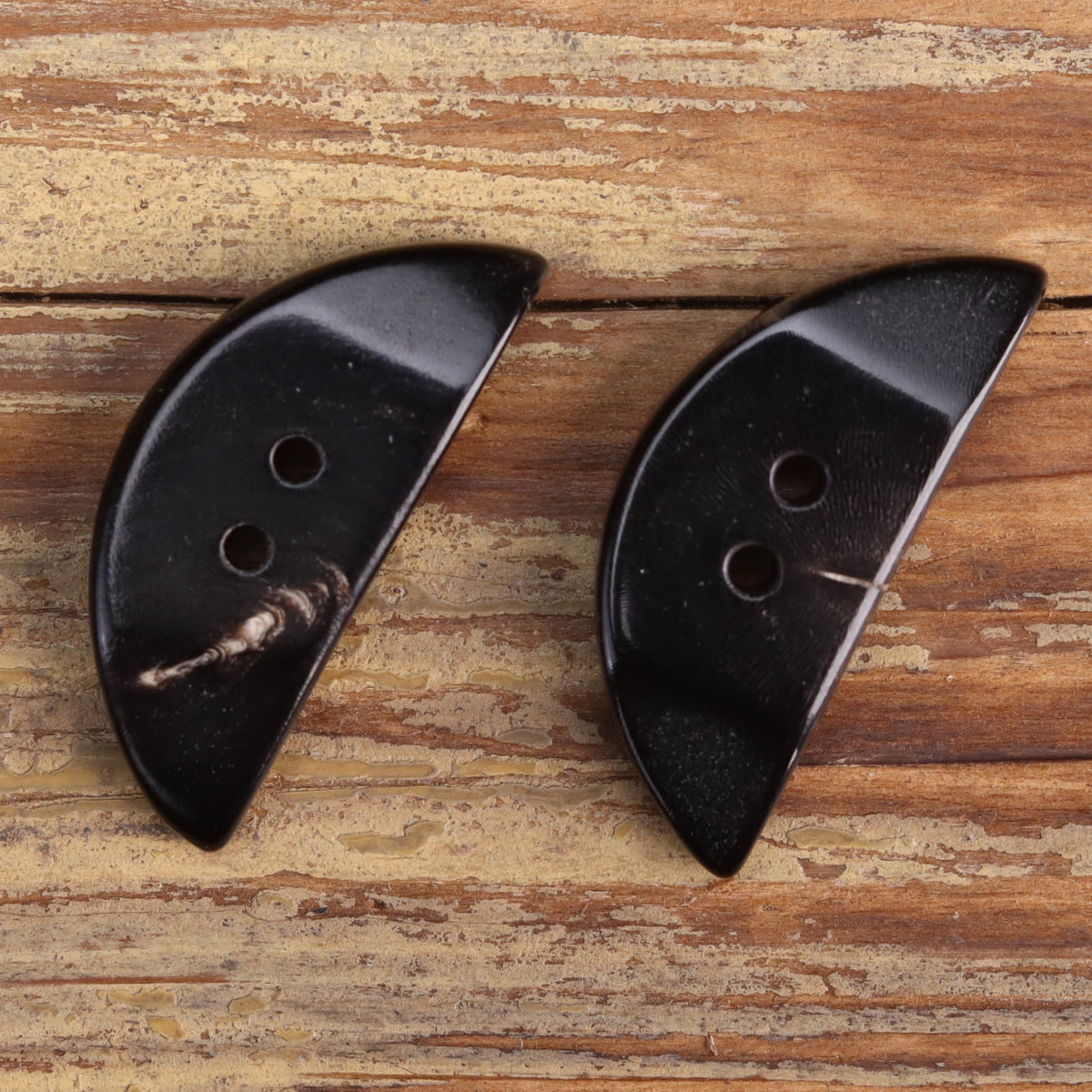 Two black irregular triangular horn buttons with multiple round holes