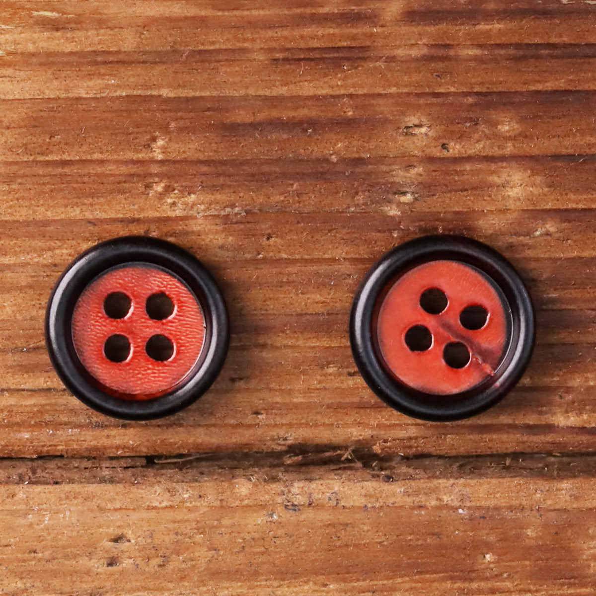 Two red round shirt buttons with black edges and four holes each