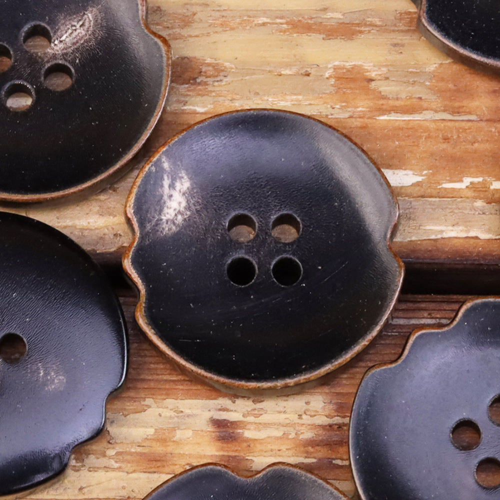 Close-up dark irregular natural horn-look button with 4 holes and textured finish
