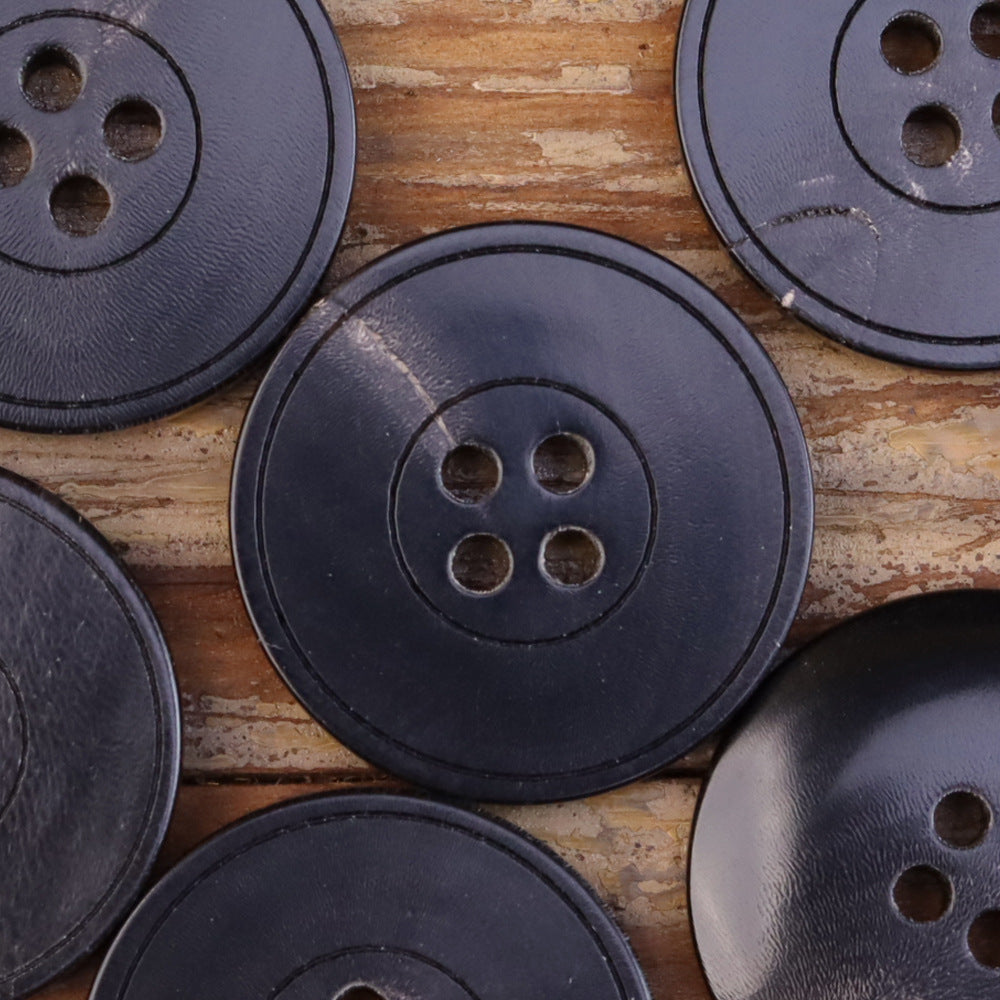 Close view of dark 4-hole flat jacket horn buttons, subtle grooved ring lines (set).