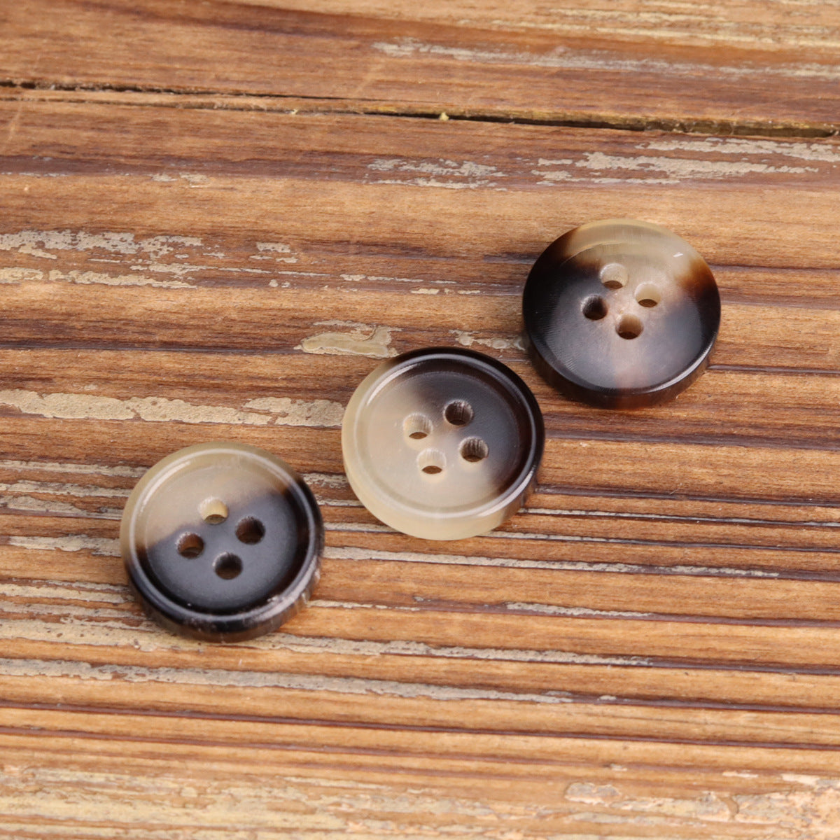 Three round 4-hole shirt buttons in amber and dark horn tones