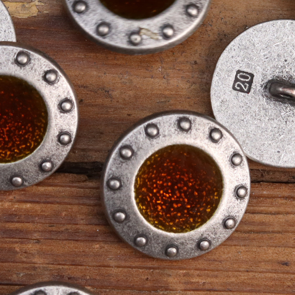 Close-up of metal sew-on buttons with brown and green glitter centers; studbed round rim