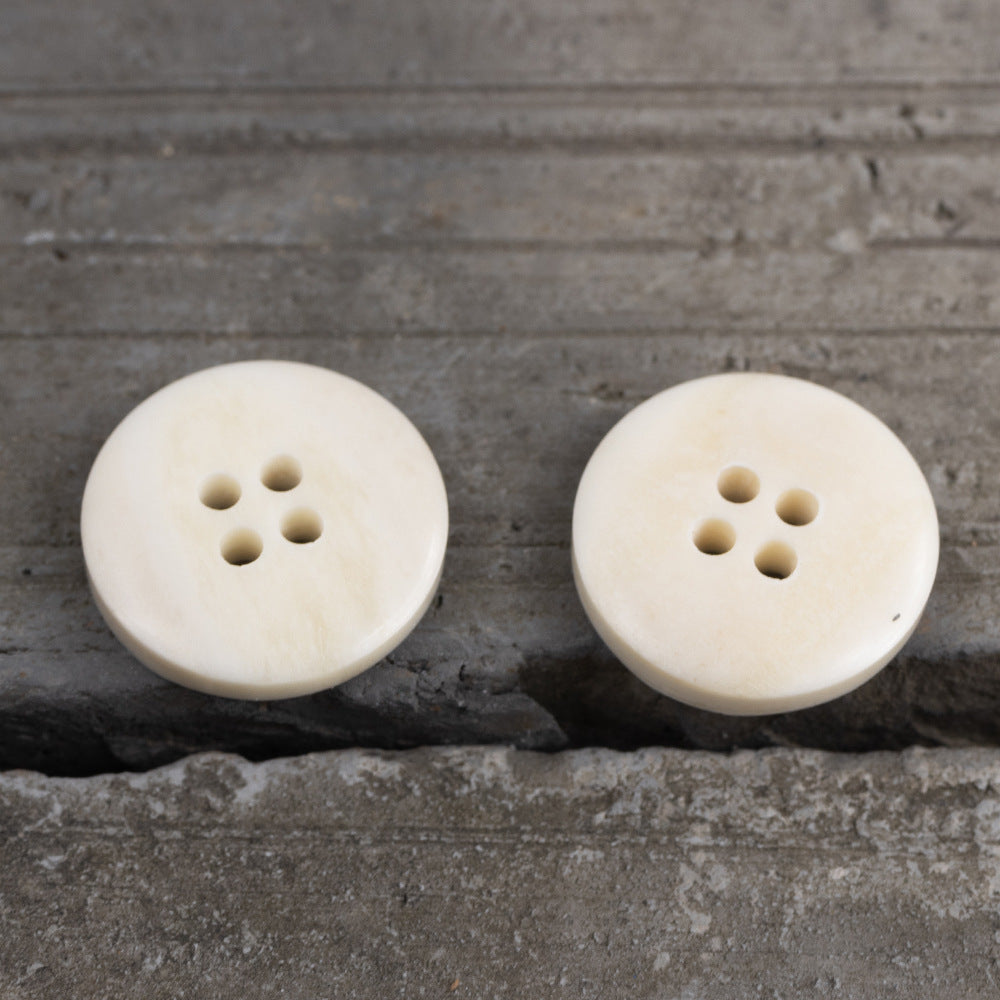 Cream round 4-hole button, smooth surface with four stitched holes