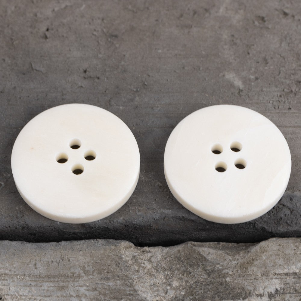 Two off-white 4-hole buttons with wide rim, front view