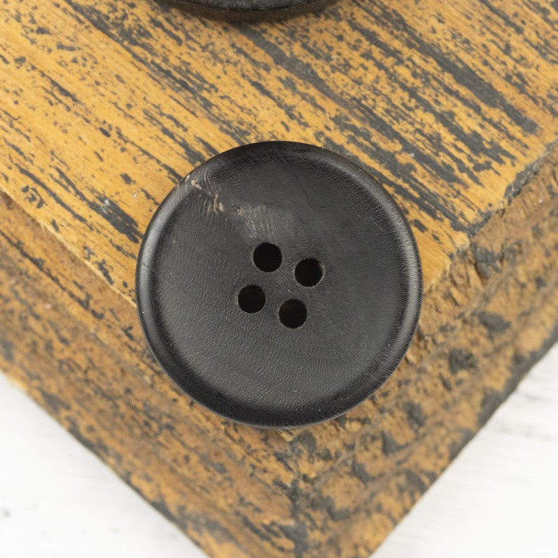 Matte black four-hole horn-style button, close-up front
