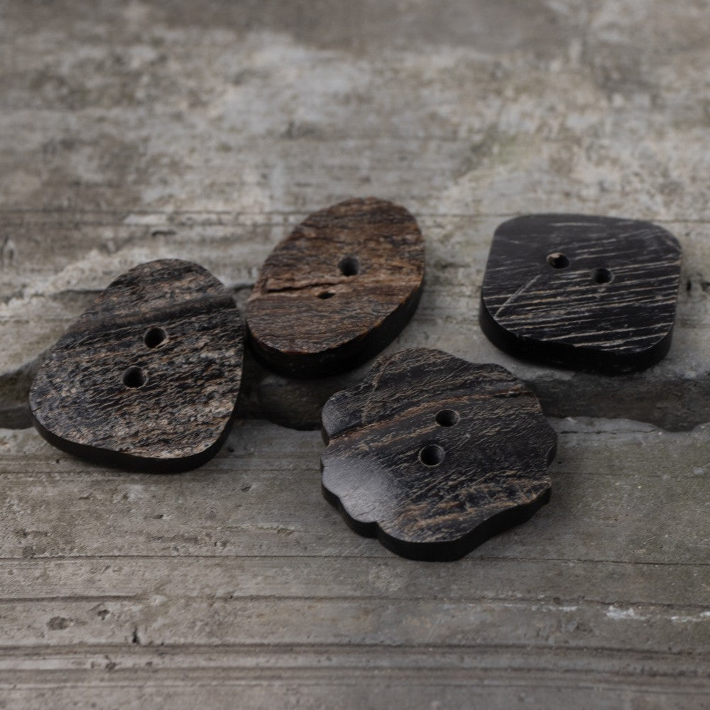 Assorted black horn buttons with two holes: rounded oval, square, and triangle shapes