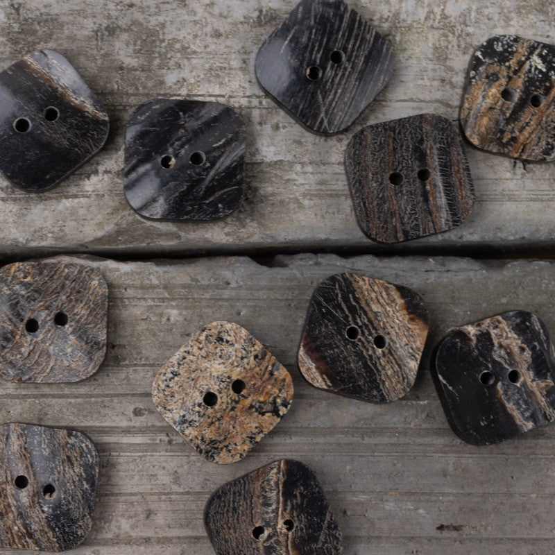 Group of black horn buttons with two holes, assorted shapes with visible grain