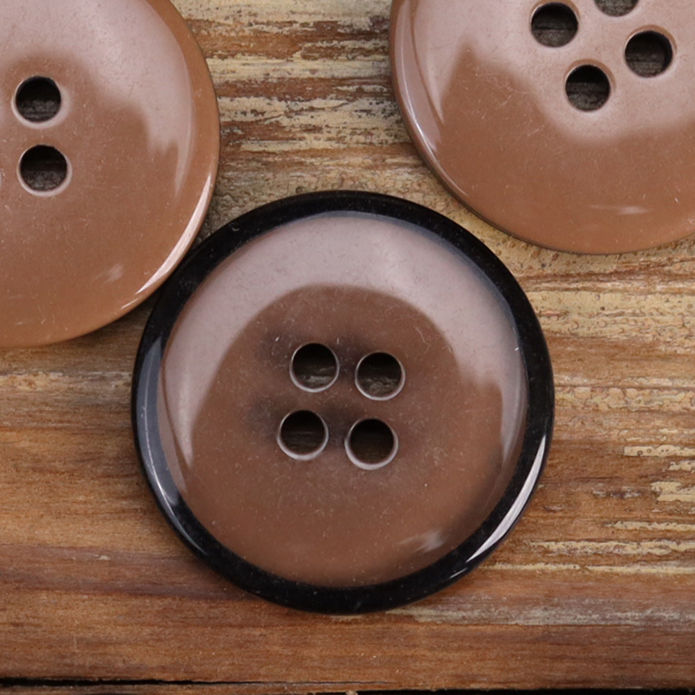 Close-up transparent resin four-hole button in brown with black rim and visible stitching holes
