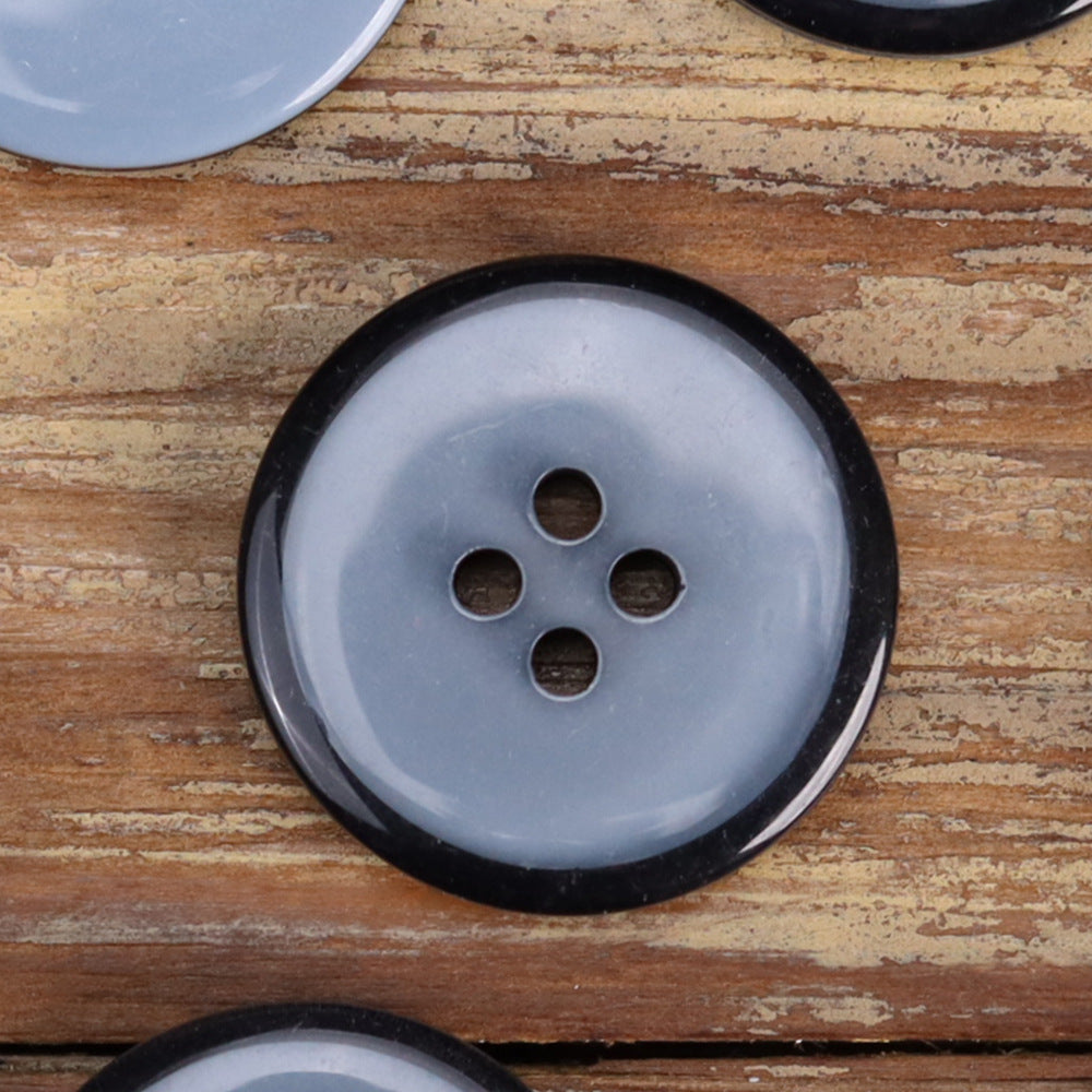 Close-up transparent resin four-hole button in light blue with black rim, jacket button