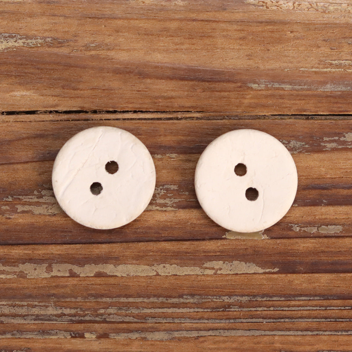 Pair of natural white 2-hole wooden buttons, two dark holes visible