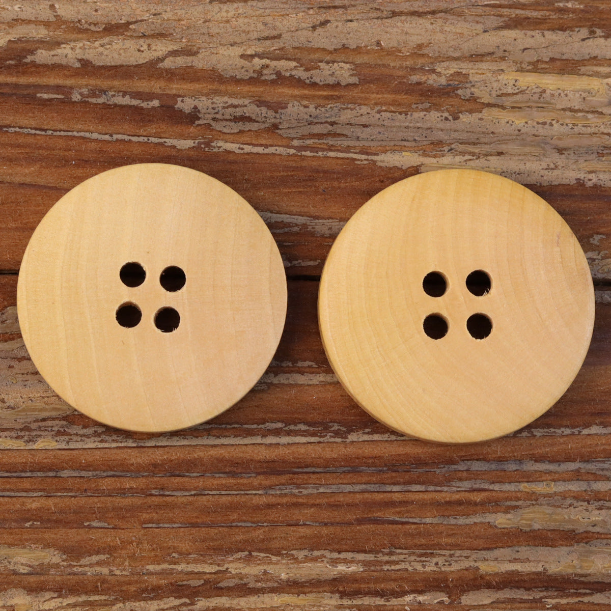 Two natural round 4-hole wood buttons on surface, light tan wood grain