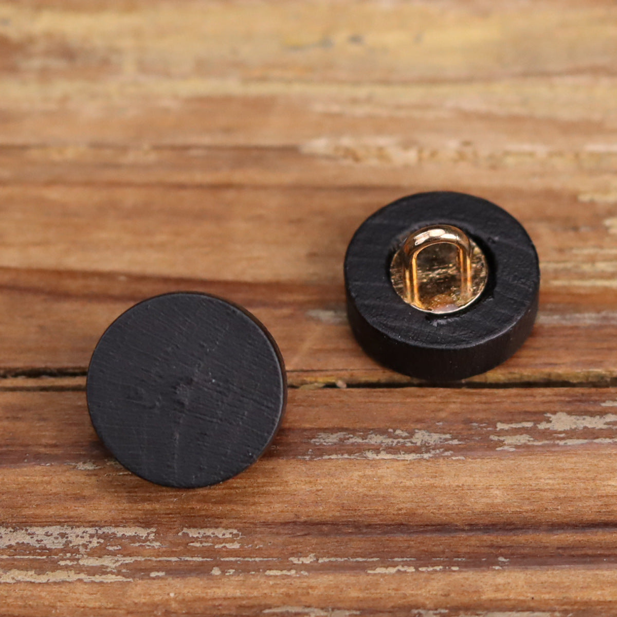 Black wooden buttons with gold-toned metal loops, front view on wood surface