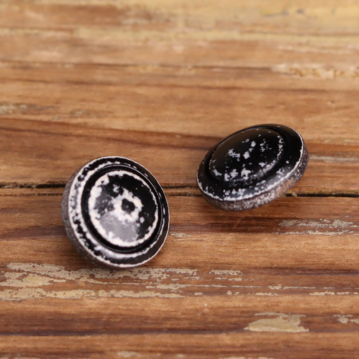 Pair of distressed black-and-white lacquered wooden buttons, one top-down and one side view