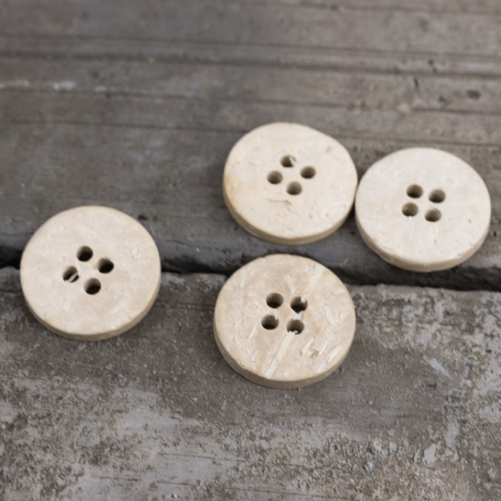 Four round off-white flat buttons with four-hole pattern and mottled surface